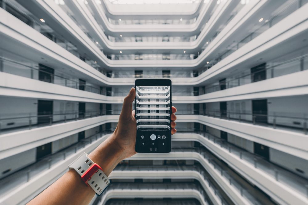 Person holding a phone in the atrium of a large office building - mingwei-li-461148