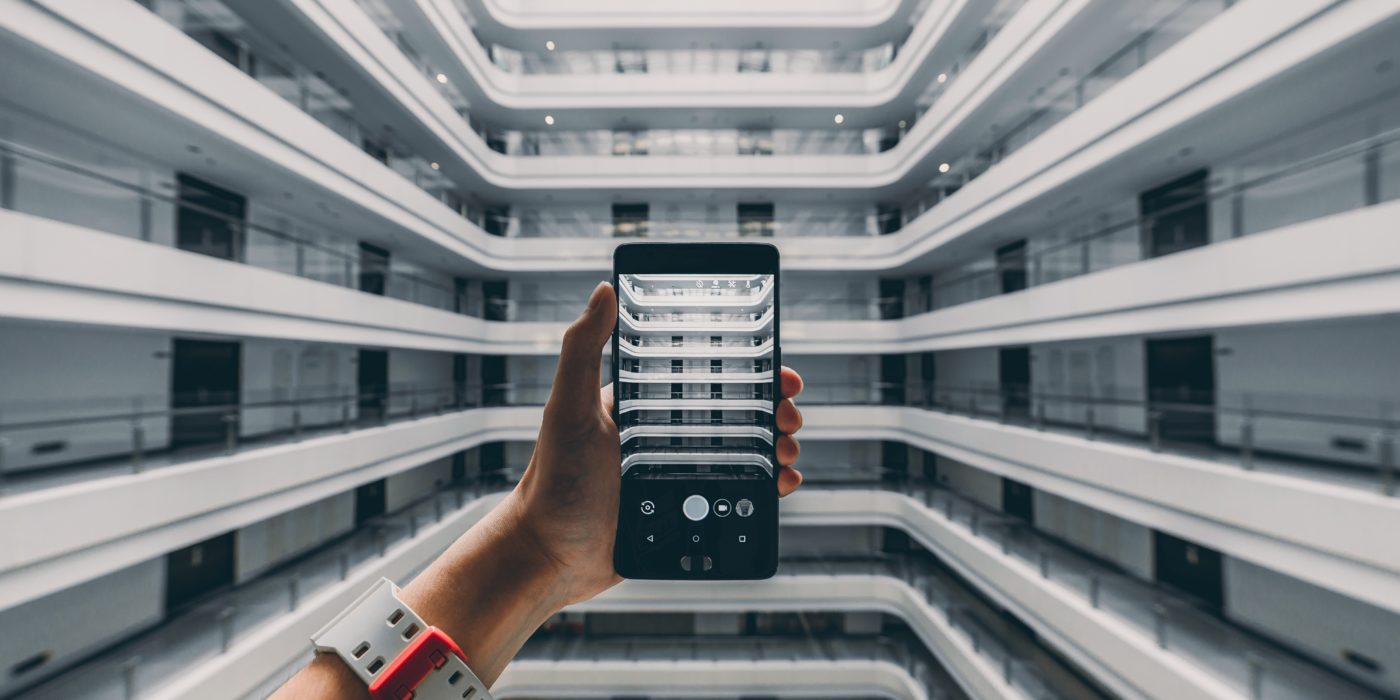 Person holding a phone in the atrium of a large office building - mingwei-li-461148